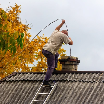 Technician sweeping a chimney flue from the rooftop using a cleaning rod.