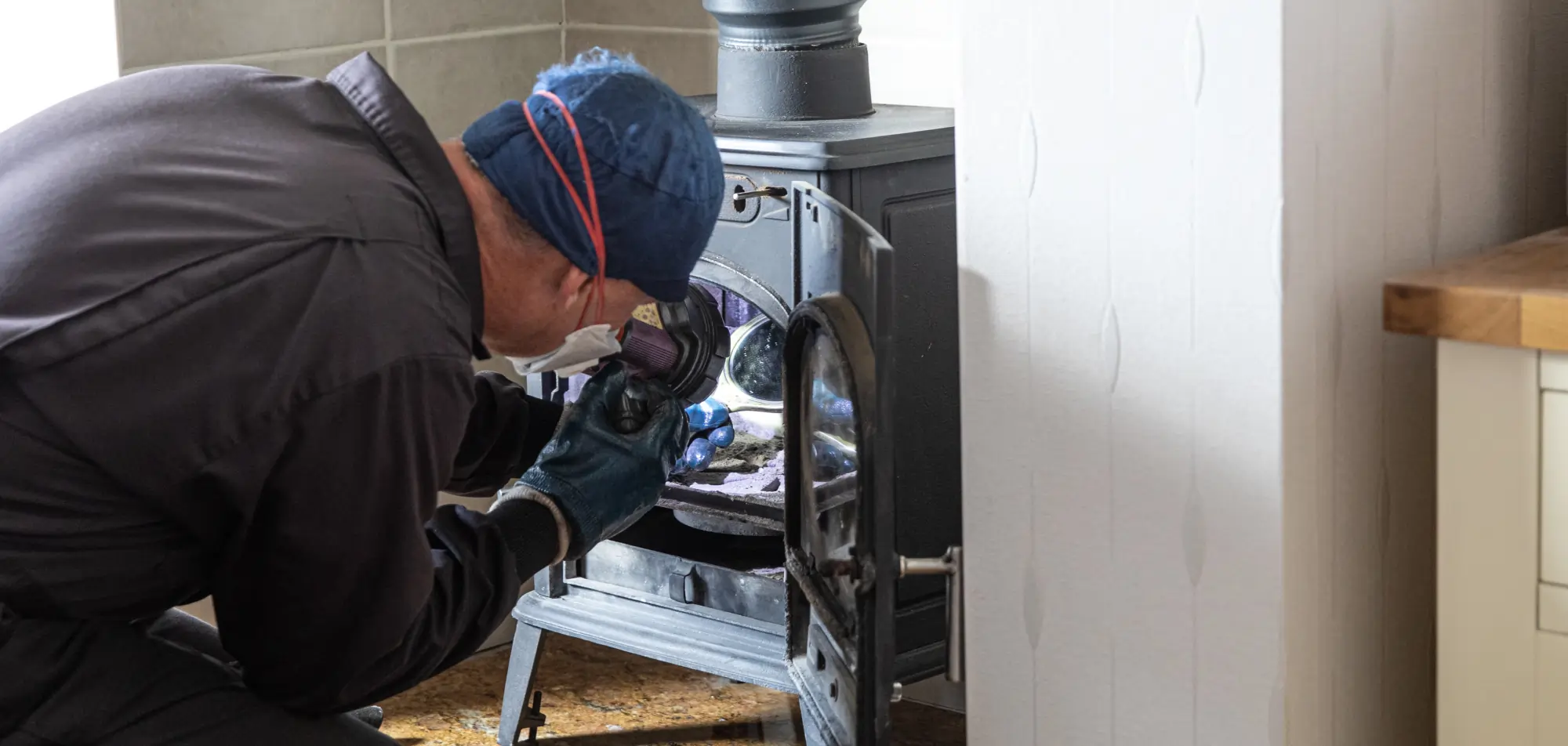 Technician performing a detailed fireplace inspection inside a wood stove firebox