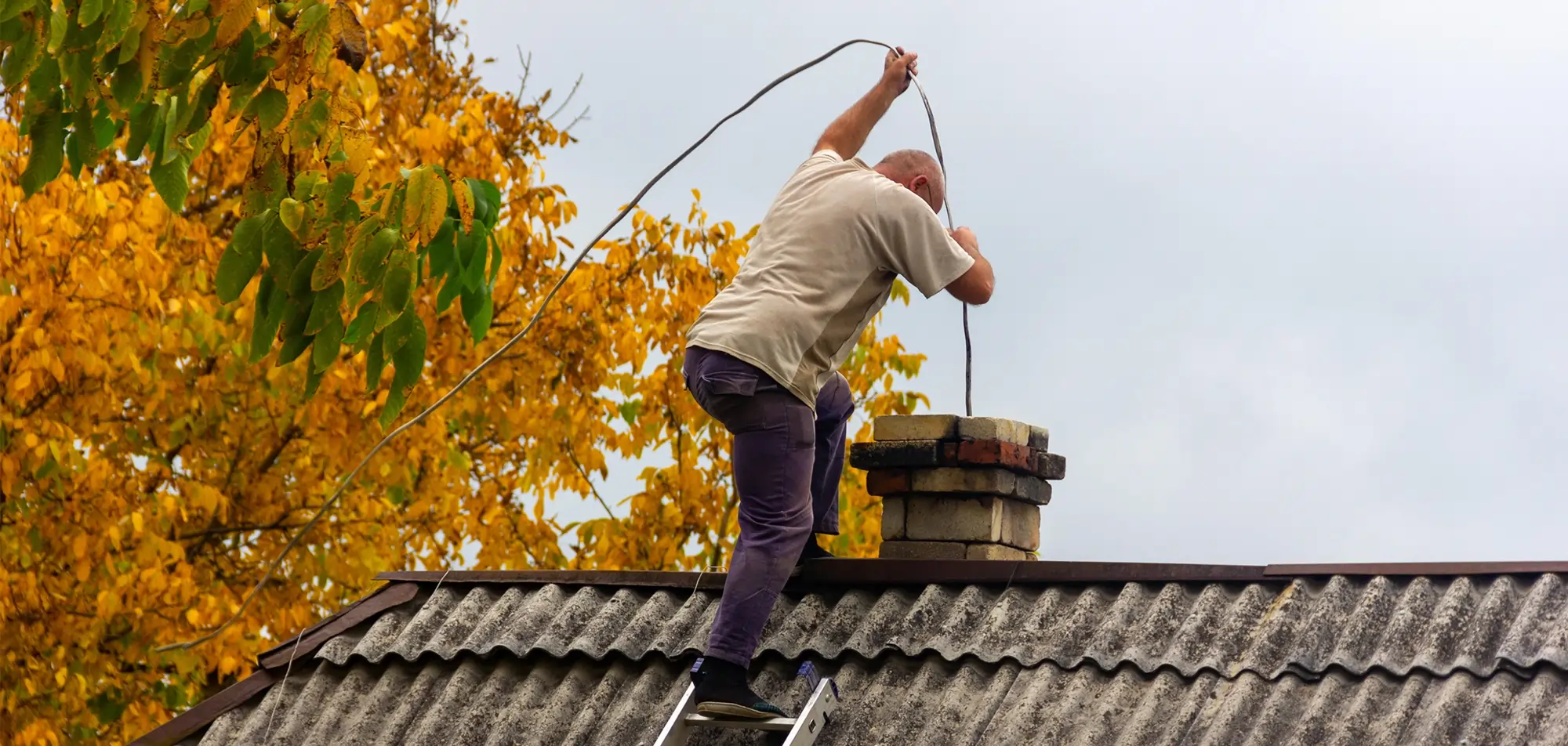 Chimney sweep cleaning the flue from the roof using professional chimney brushes