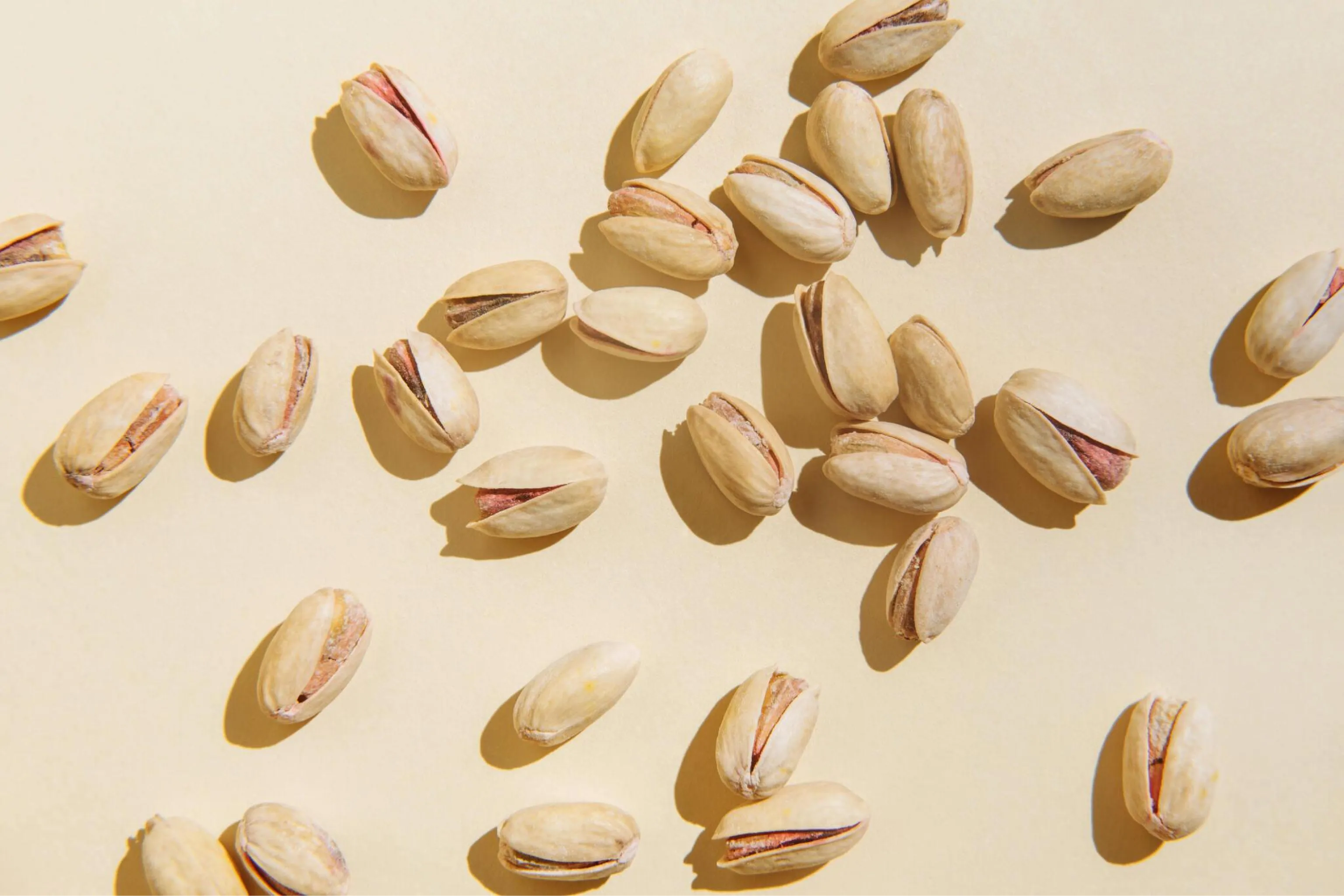Scattered pistachio shells on a warm cream background, with sunlight casting soft shadows in a natural overhead composition, evoking calm.