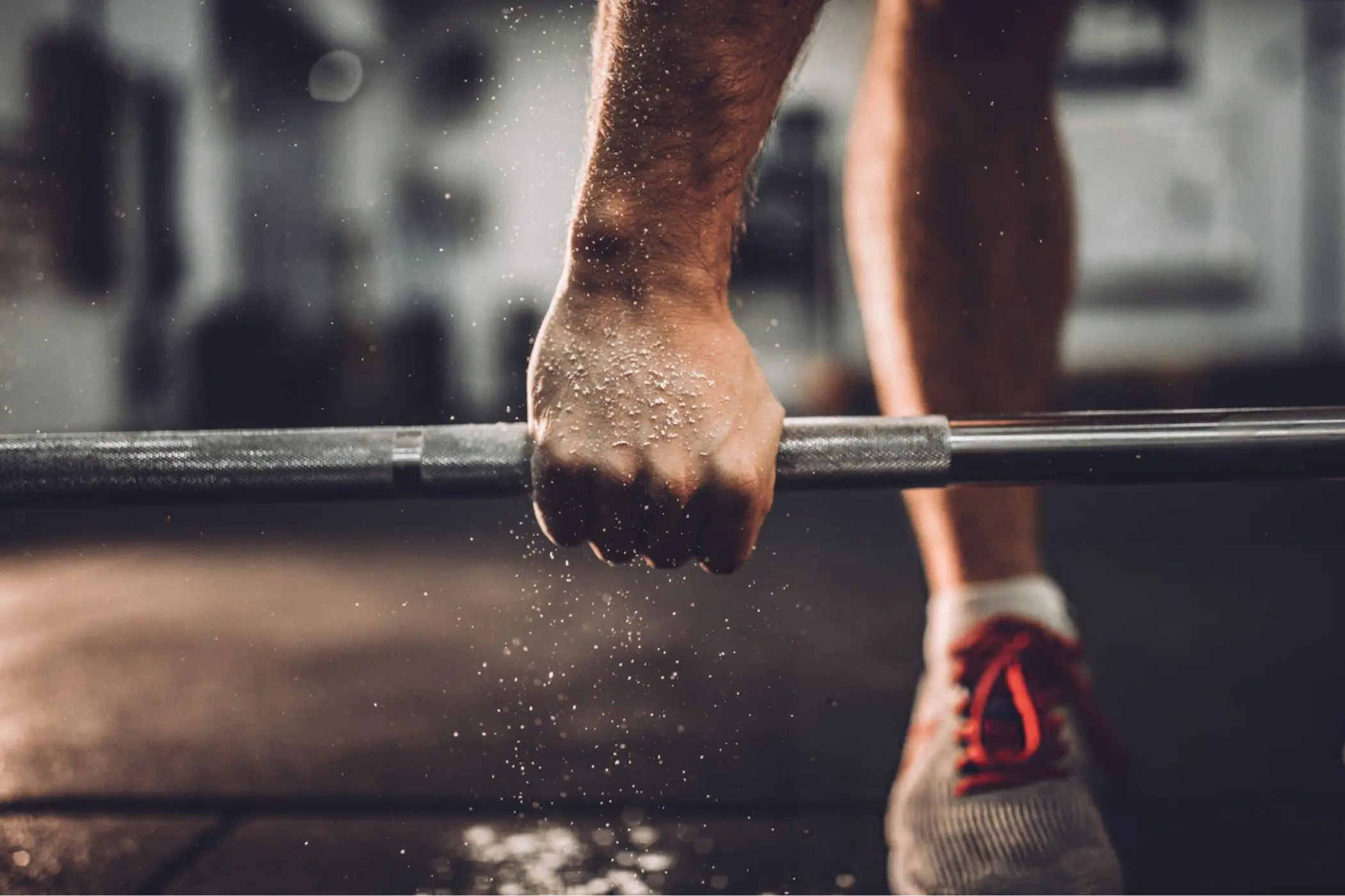 Close-up of a sweaty athlete gripping a barbell in a gym, chalk dust falling from the hand; dramatic lighting conveys strength and focus.