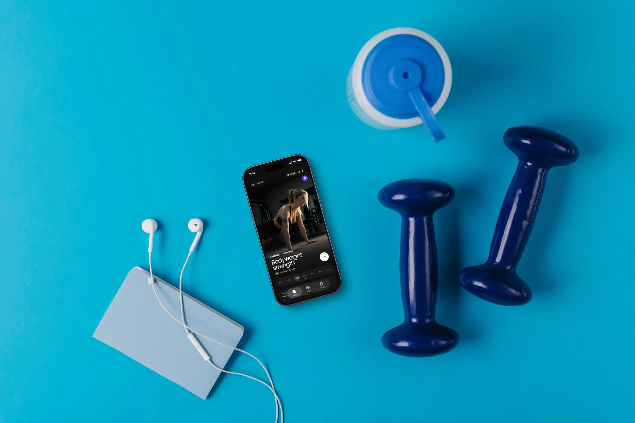 A music-playing smartphone, white earbuds, blue face mask, drink cup, and two dumbbells arranged on turquoise, suggesting an upbeat home workout.