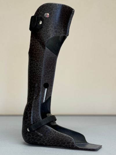 Leopard print leg brace with black straps and padding, standing upright on a flat surface.