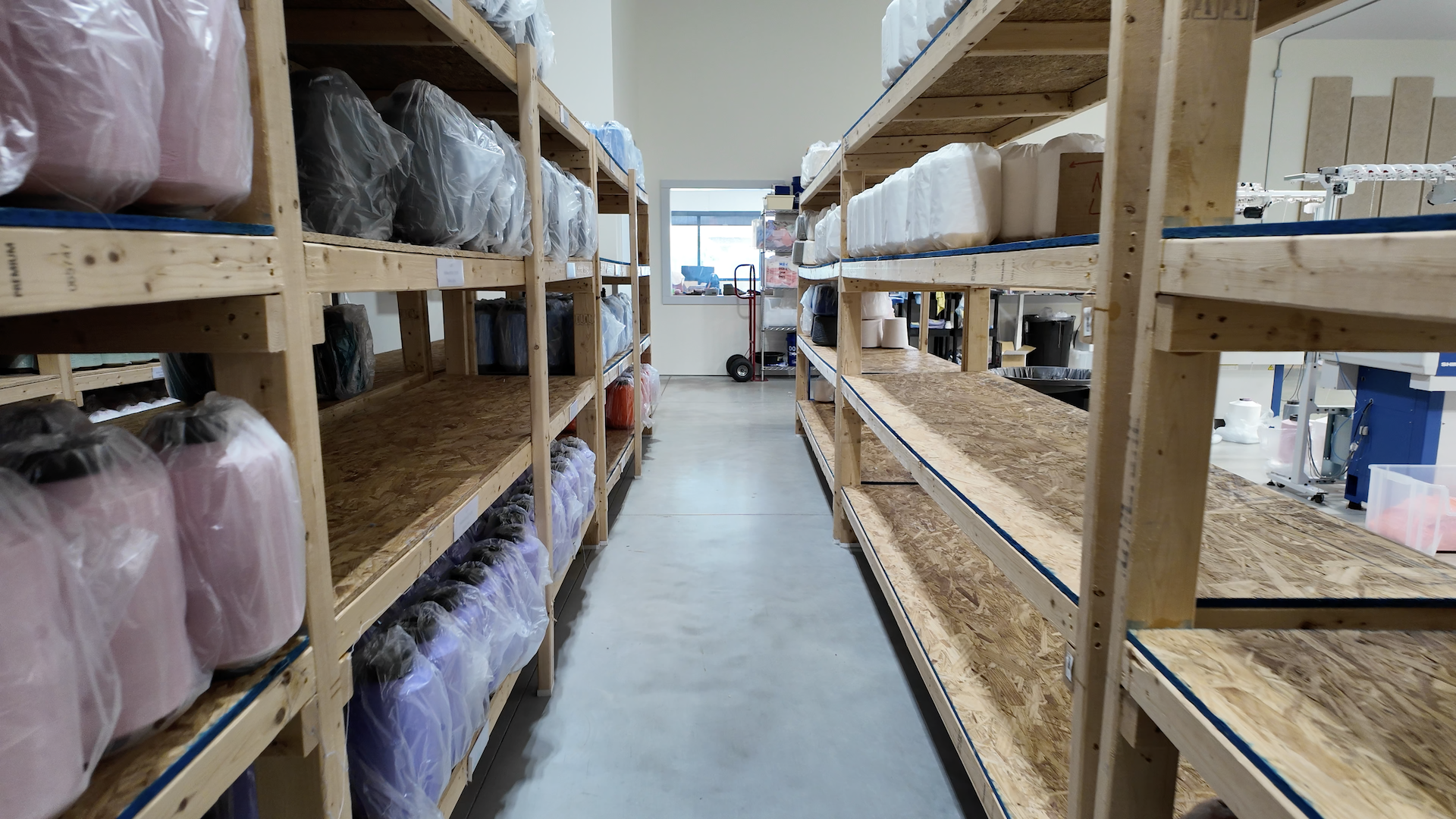 Interior view of KnitIt's manufacturing facility showing organized shelves stocked with fabric materials used to create Swaddelinis, demonstrating the company's commitment to local production.