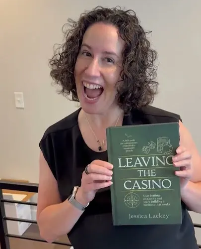 Jessica Lackey smiling and holding her book "Leaving the Casino" which has a green cover with decorative illustrations and her name at the bottom.