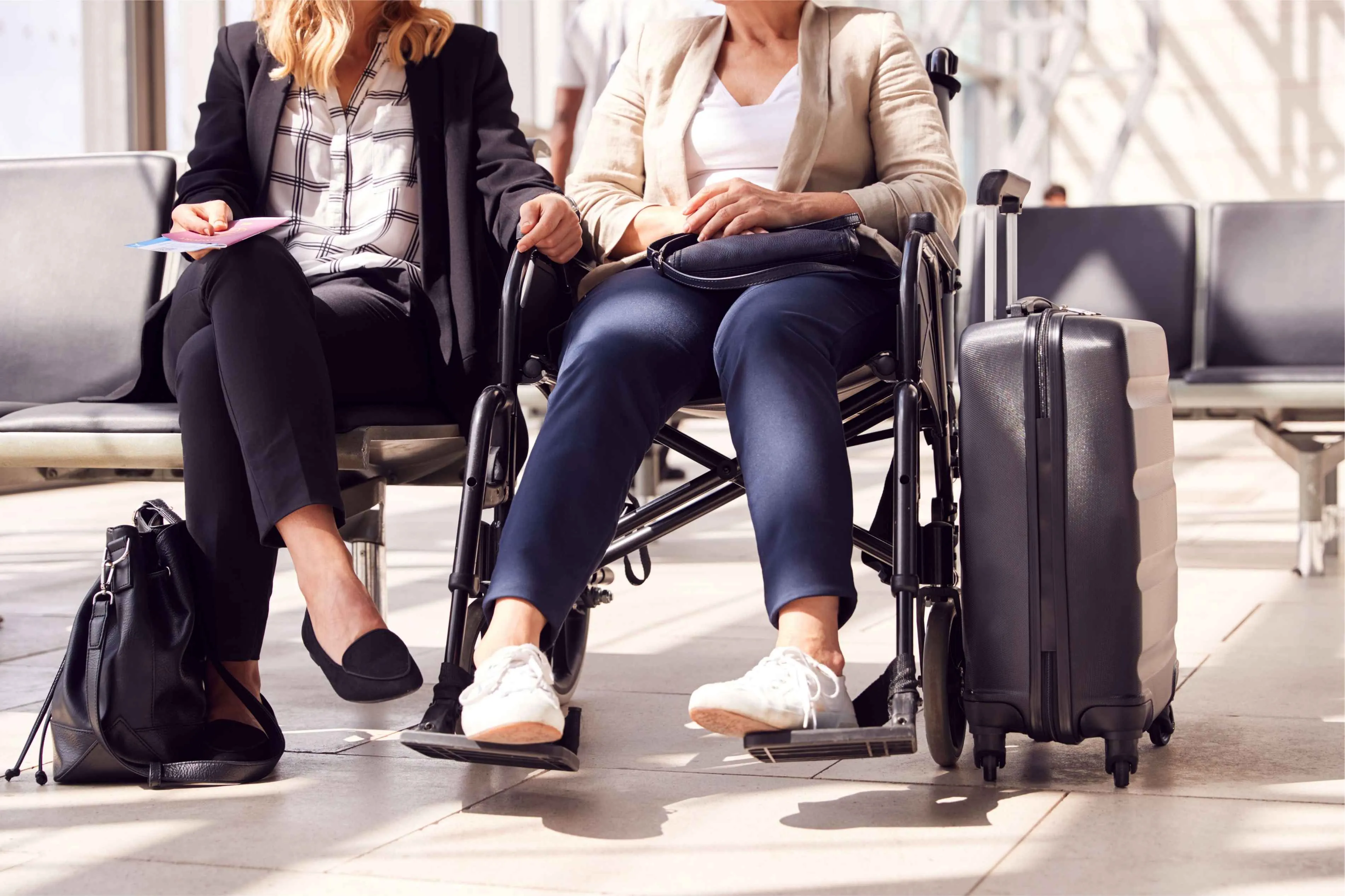two women sitting in an airport with suitcases, one of whom is in a wheelchair