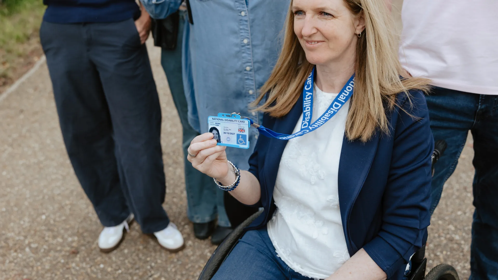 Photo of a woman in a wheelchair holding up her National Disability Card on its lanyard.