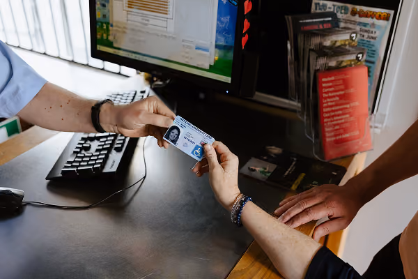 Photo of someone holding out their National Disability Card at a ticket counter, which is accepted by the staff member on the other side