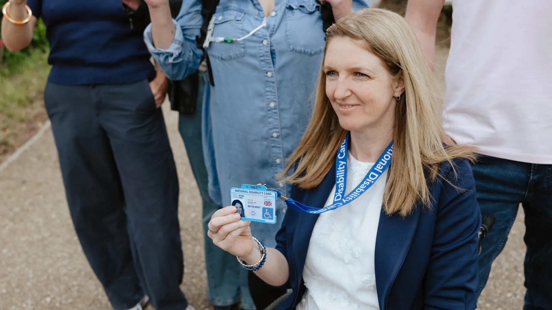 Photo of a woman in a wheelchair holding up her National Disability Card on its lanyard.