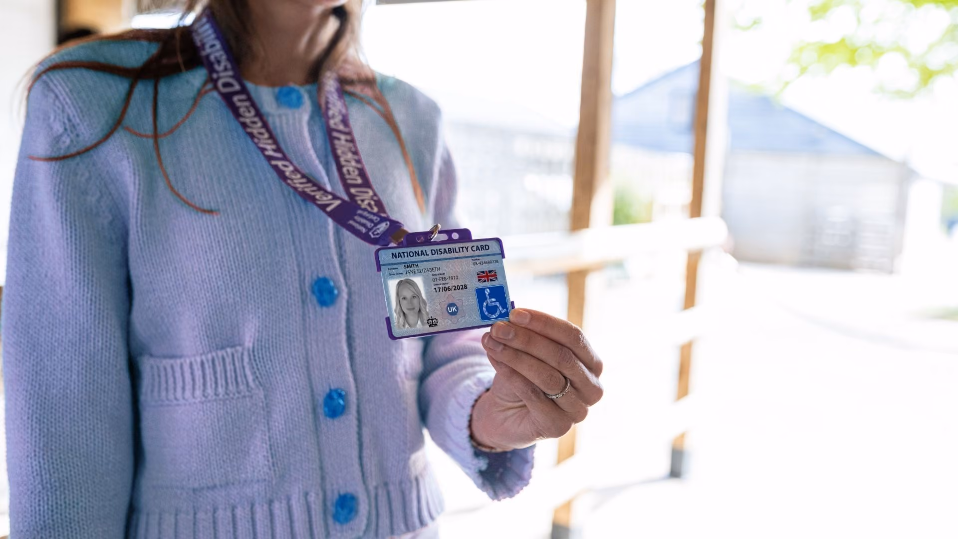 Photo of a woman in a wheelchair holding up her National Disability Card on its lanyard.