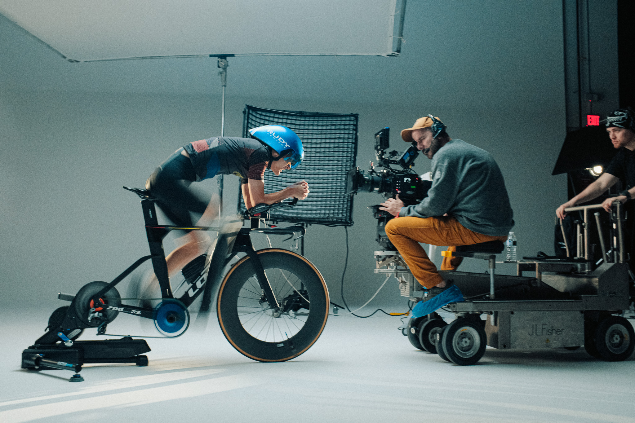 Cyclist Kai riding on a trainer as DP Joe Sailer films from a J.L. Fisher dolly on the Slow Down To Speed Up set