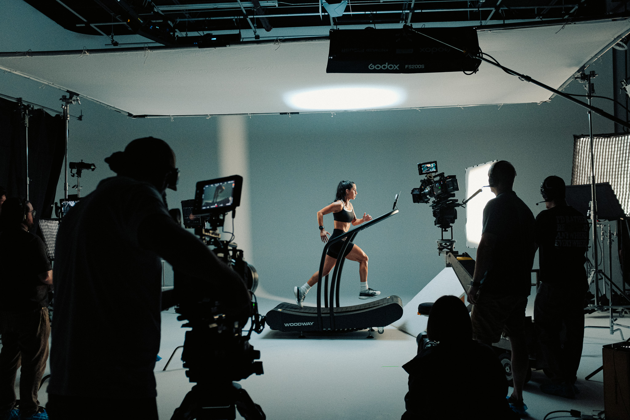 Runner Lesly on a curved treadmill on the cyc wall, framed by silhouetted crew and cameras