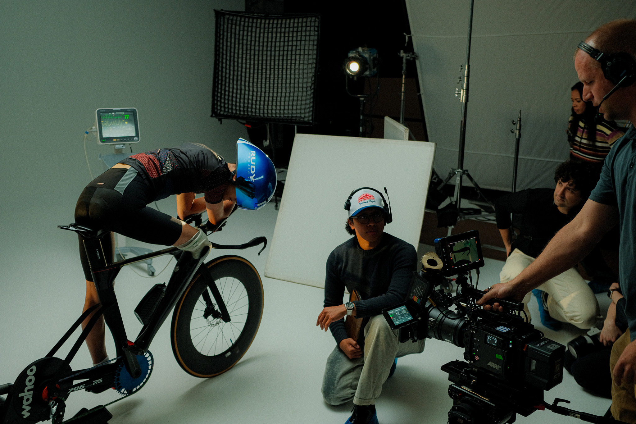 Director kneeling beside the ARRI camera as Kai rides the trainer in an aero tuck