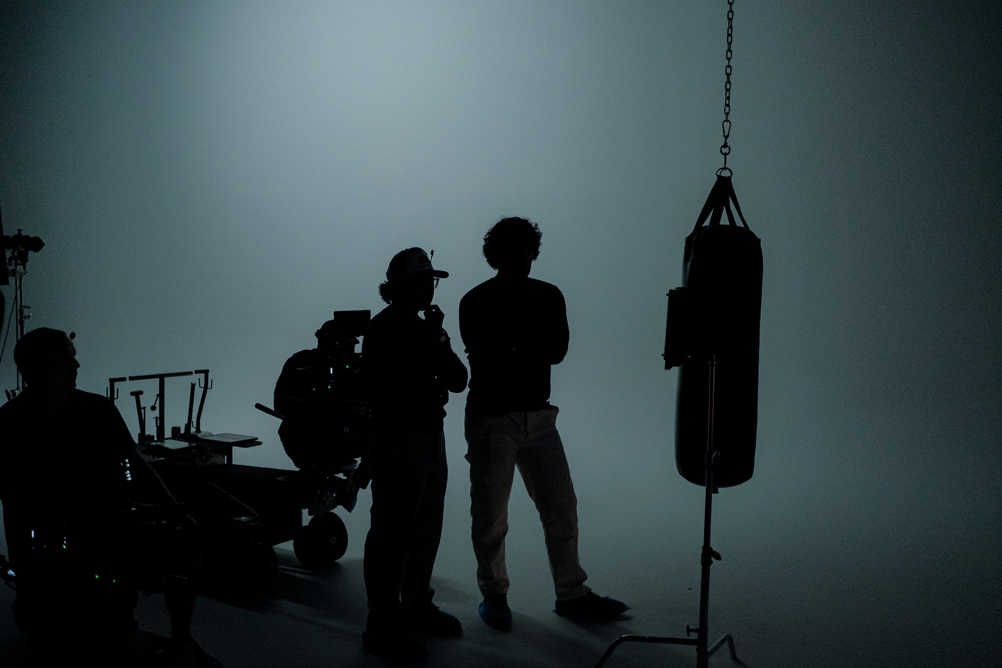Chris Vergara and a collaborator in silhouette talking beside the heavy bag on set