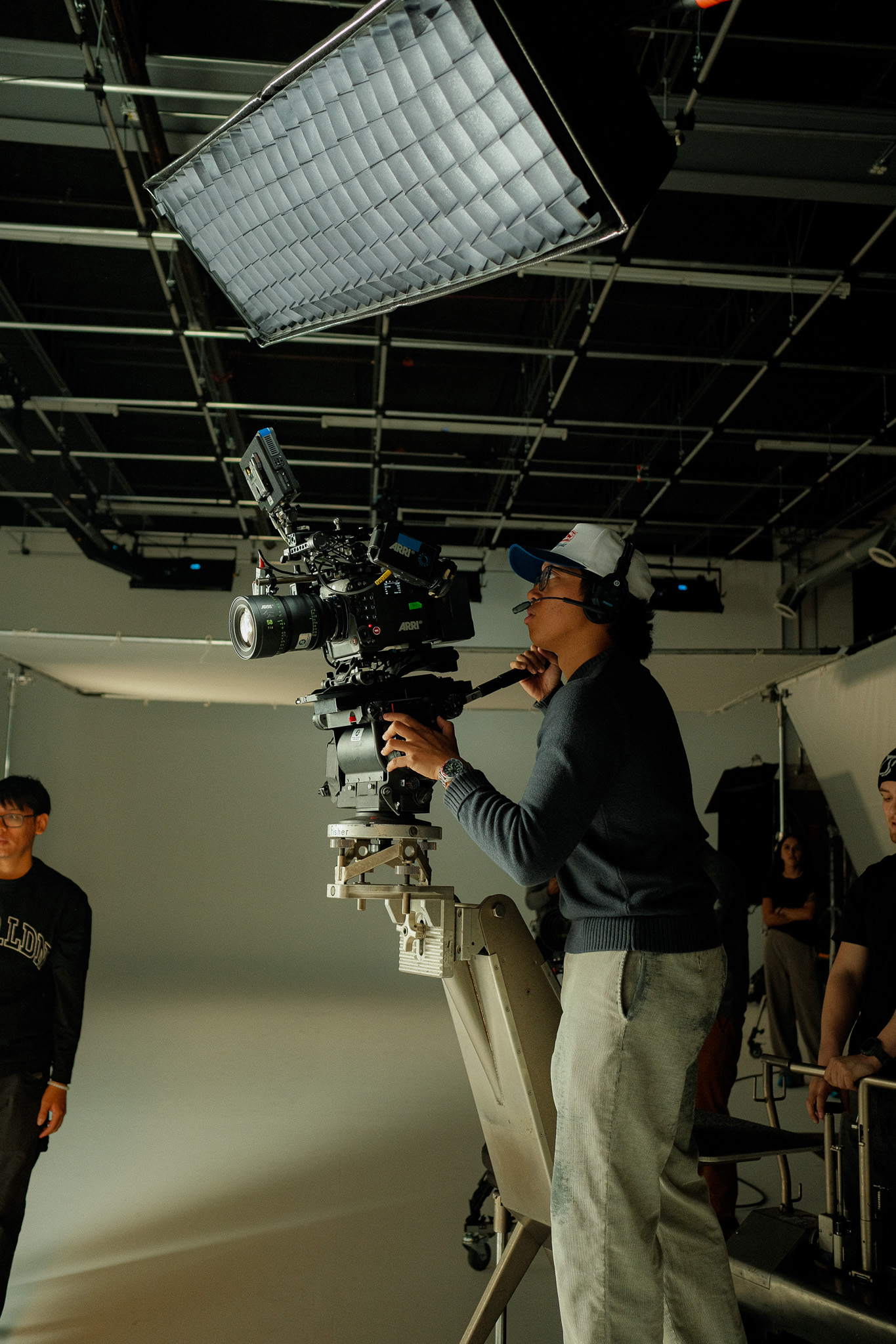 Camera operator on the dolly arm framing up under a gridded softbox
