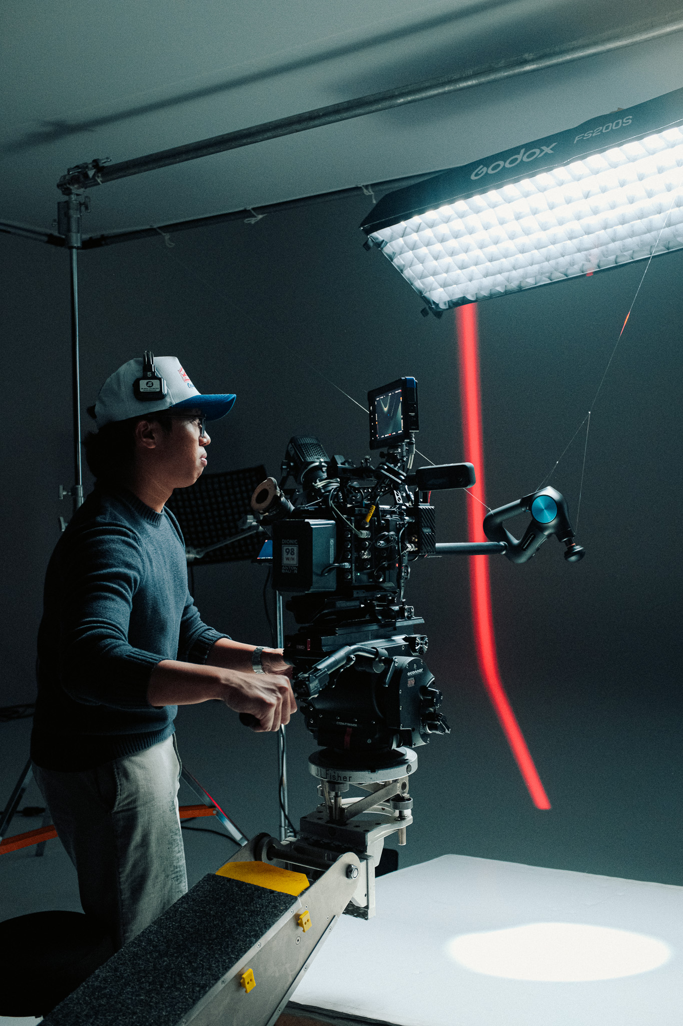 Camera operator on the dolly with a Theragun rigged off the front of the camera