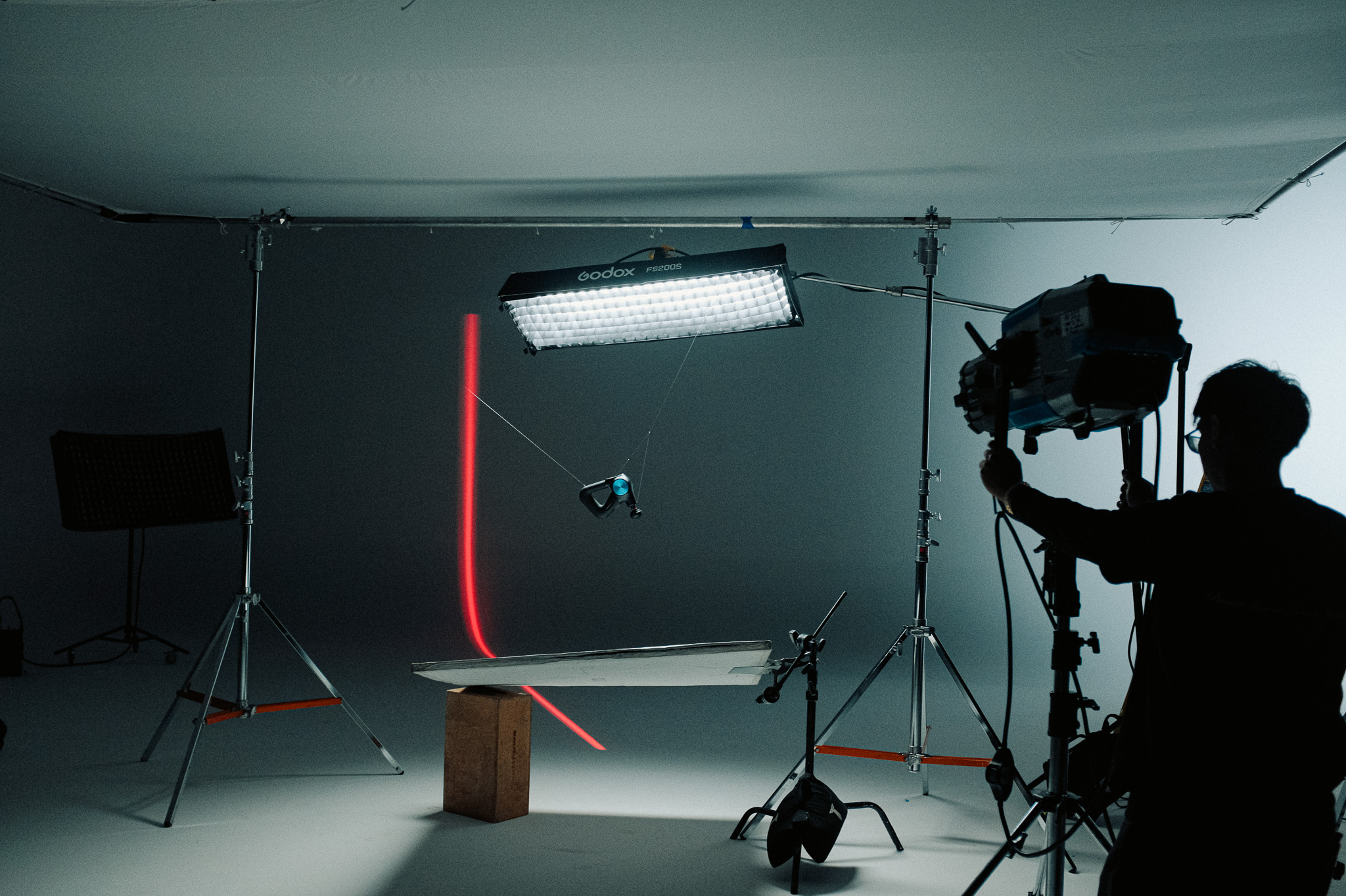 A Theragun suspended on fishing line under a gridded softbox with a red light streak behind