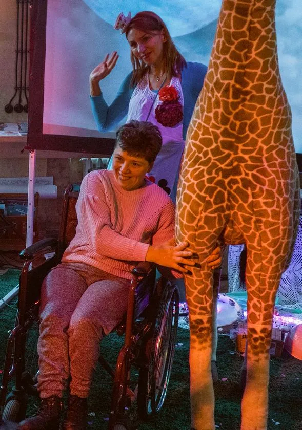Frau im Rollstuhl mit Assistentin und Plüschgiraffe beim Andreasabend