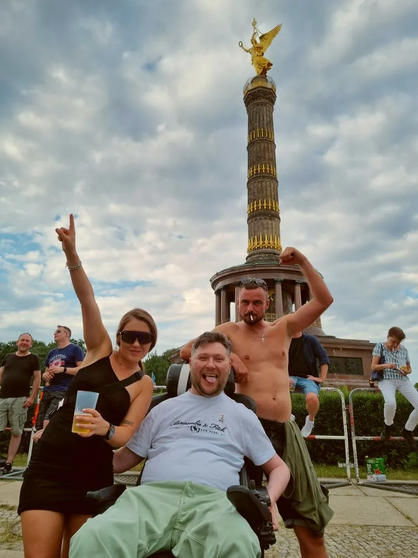 Paweł im Rollstuhl mit Freunden vor der Siegessäule in Berlin, jubelnd