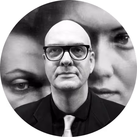 Ein Mann mit Brille vor einem Hintergrund aus Gesichtern.