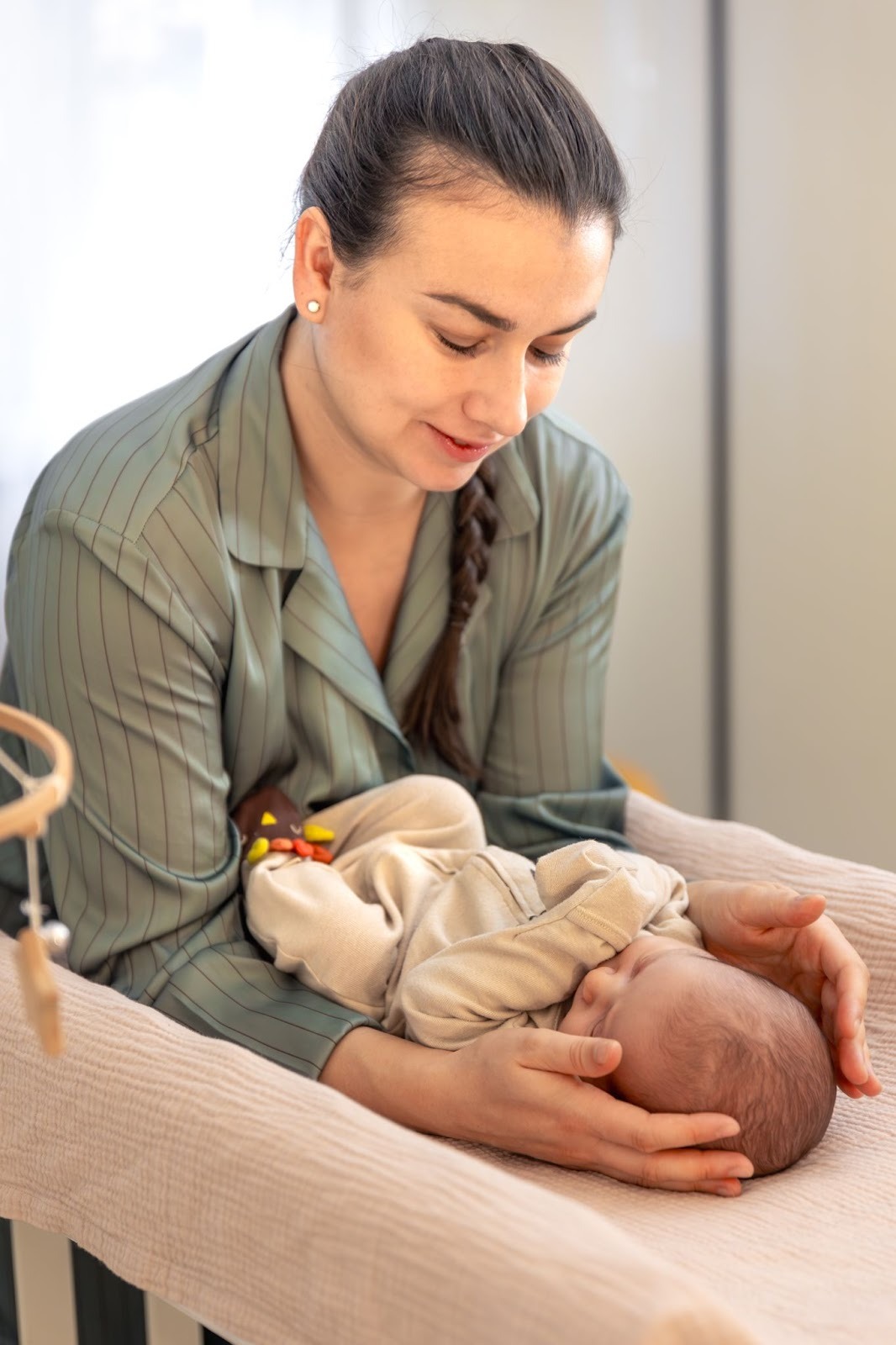 A mother gently cradles her newborn’s head while leaning over a crib—symbolizing the quiet, exhausting moments that often trigger postpartum anxiety in new moms.