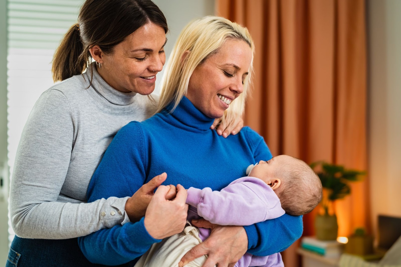 Two new mothers share a tender moment with their baby, illustrating connection and postpartum mental health support for new parents experiencing anxiety after childbirth.