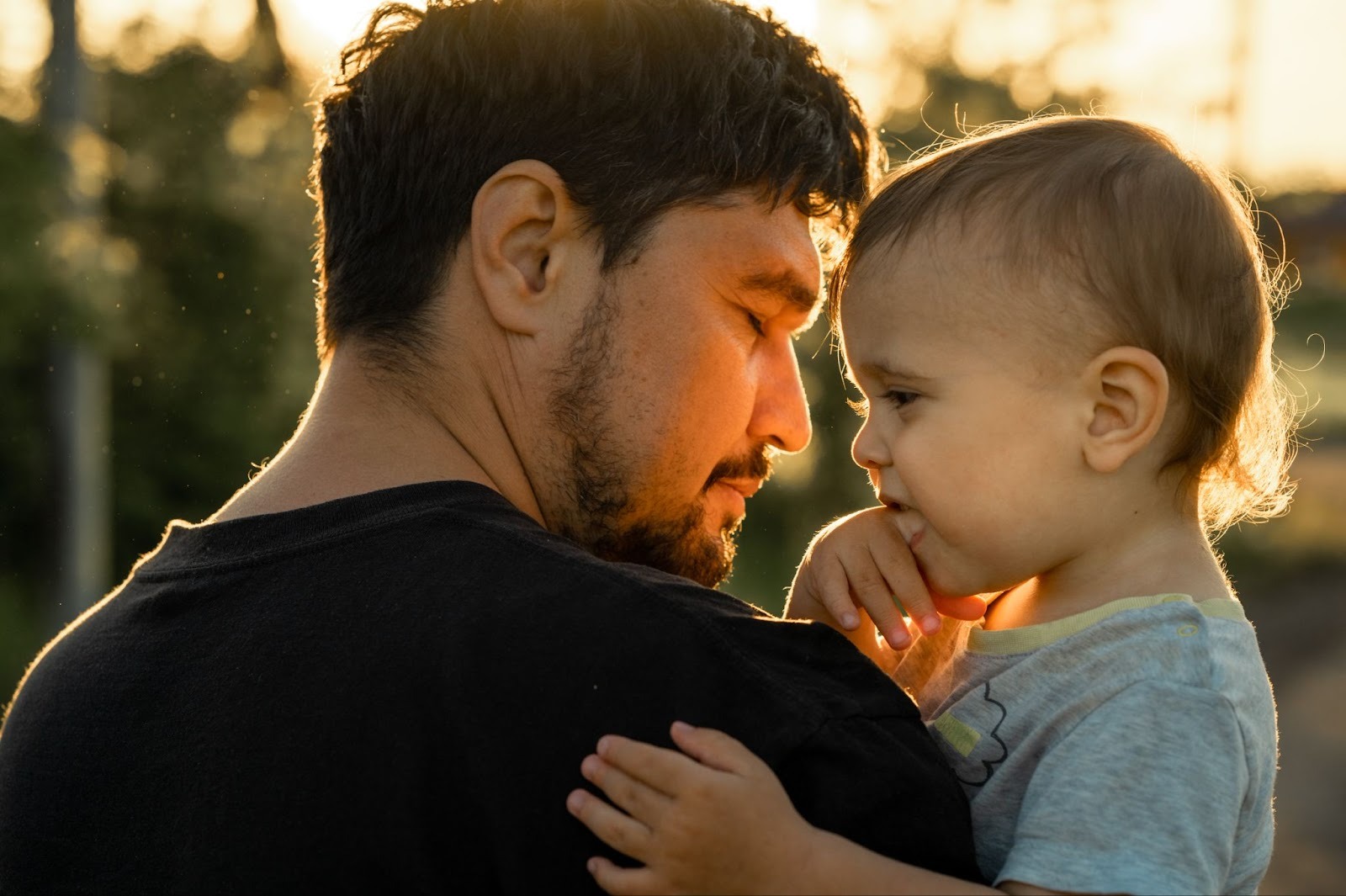 Father holding a baby outdoors at sunset, showing bonding and the emotional transition for non-birthing parents.