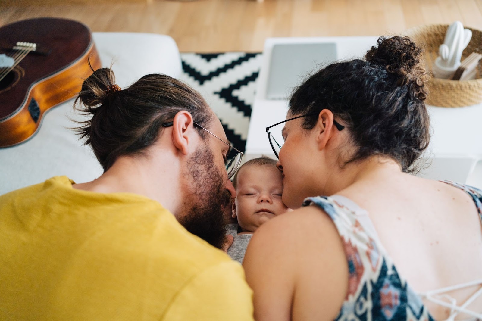 Two parents leaning close to their newborn on a bed, rebuilding connection and intimacy through postpartum couples therapy.