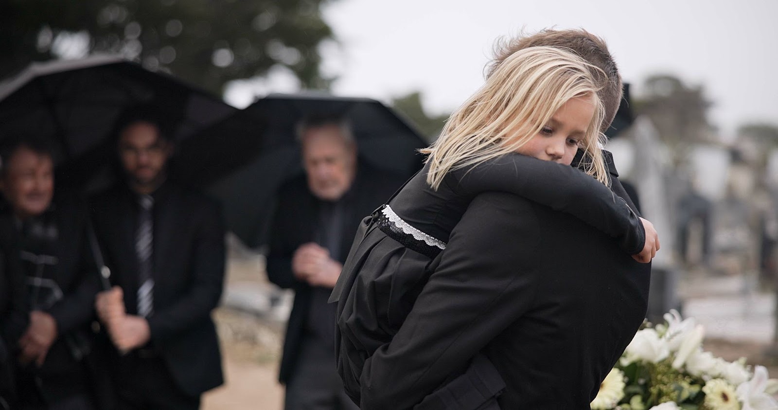 Child being comforted by a parent at a funeral, representing the pain of family loss and the role of Grief and Loss Therapy in helping loved ones process bereavement.
