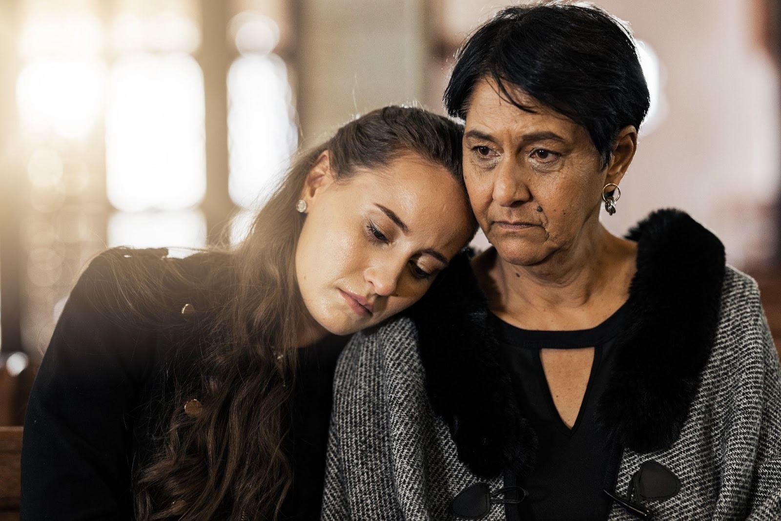 Woman resting her head on an older woman’s shoulder in a church, capturing shared sorrow, comfort, and the healing support available through grief counseling Montclair.