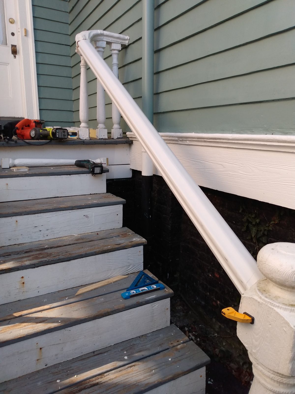 Porch steps with newly installed white handrail during rebuild