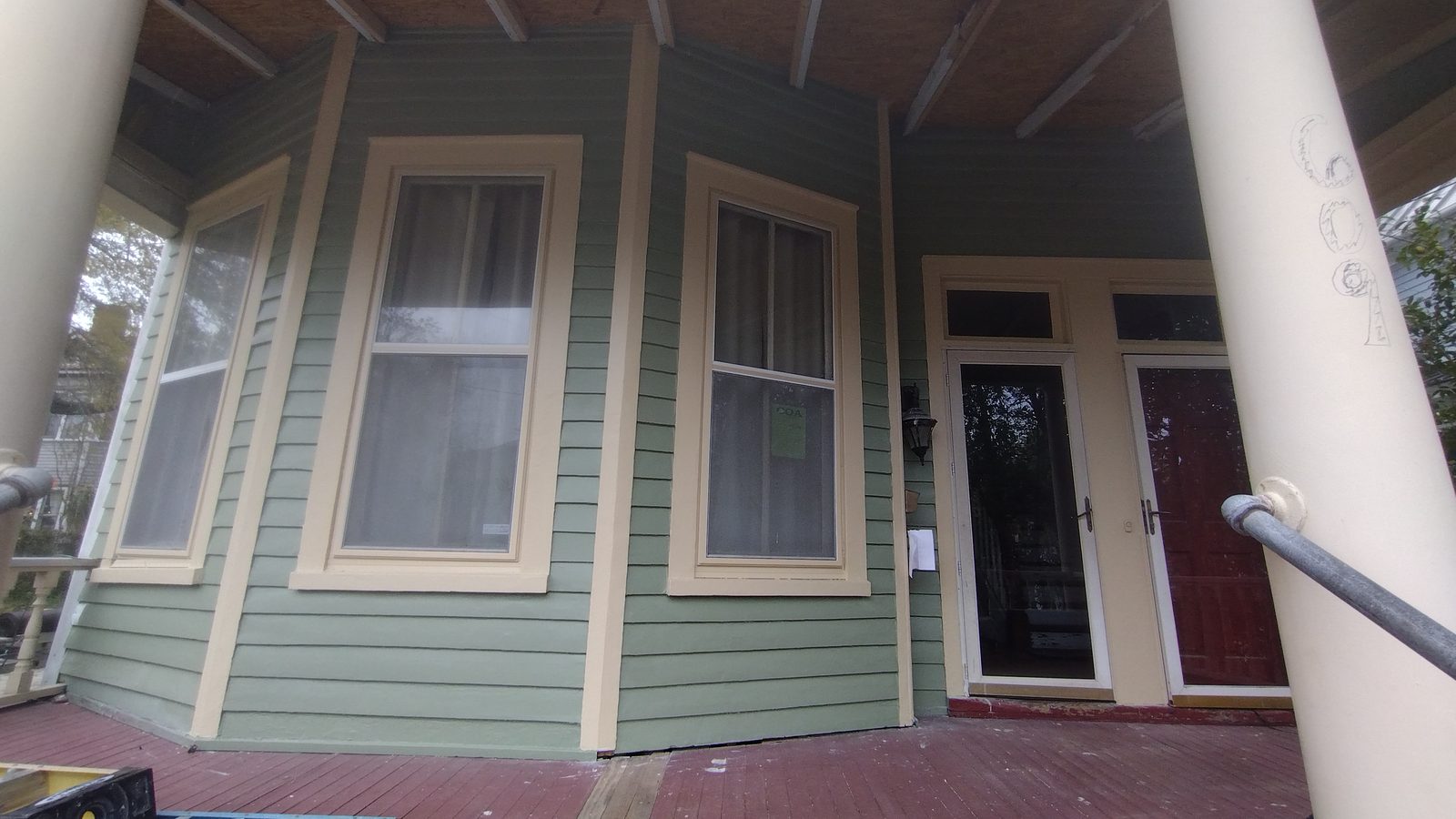 Restored Victorian porch with sage green siding, white trim, and repainted maroon deck