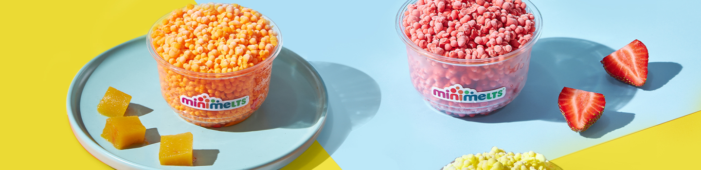 Deux gobelets Mini Melts, mangue et fraise, sur une assiette avec des fruits frais