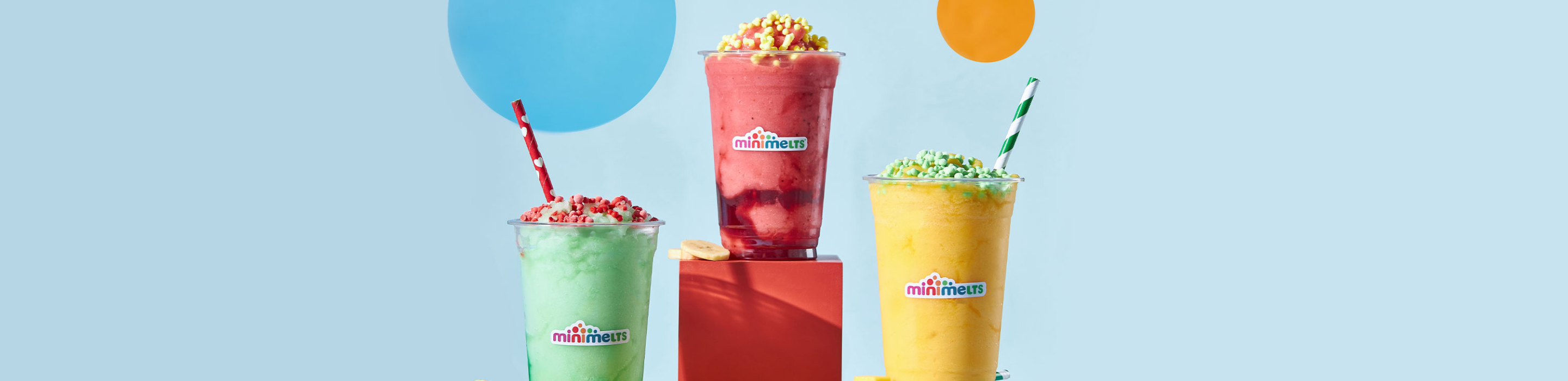 Trois smoothies Mini Melts — vert, fraise et mangue — devant un fond bleu