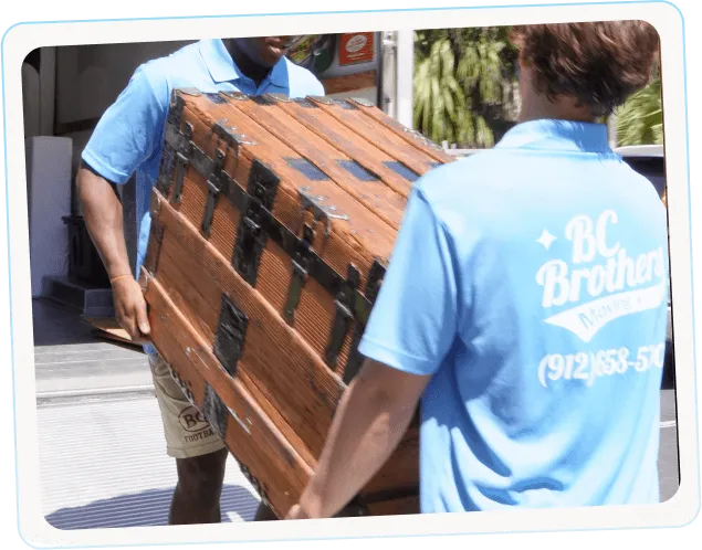 Two BC Brothers movers transporting a heavy wooden dresser during a home relocation