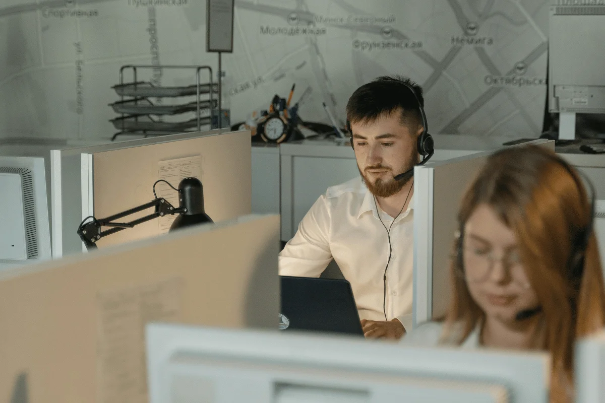 Male and female support agents working in customer service cubicles with headsets and laptops.