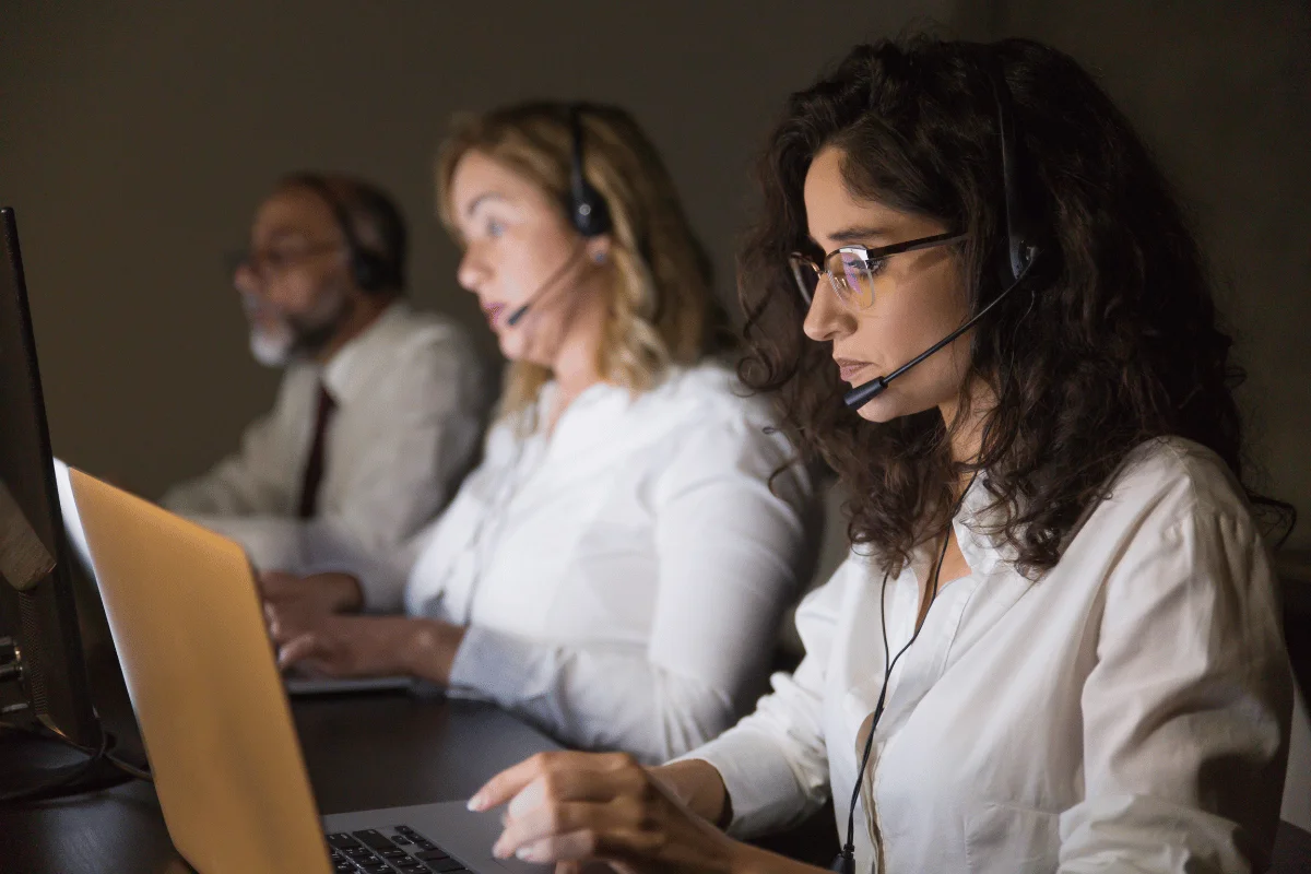 Customer service team wearing headsets and assisting clients during a late shift in a call center.