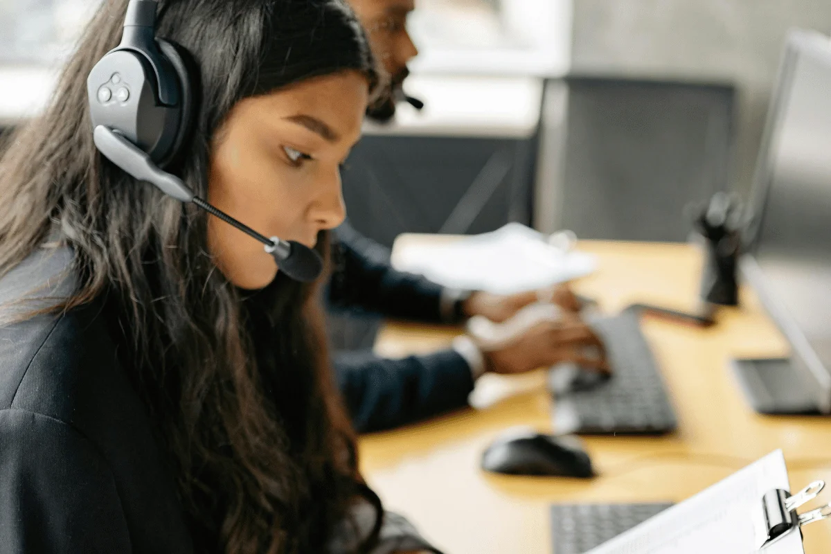 Focused call center agent reviewing paperwork while wearing headset and working at desktop computer.