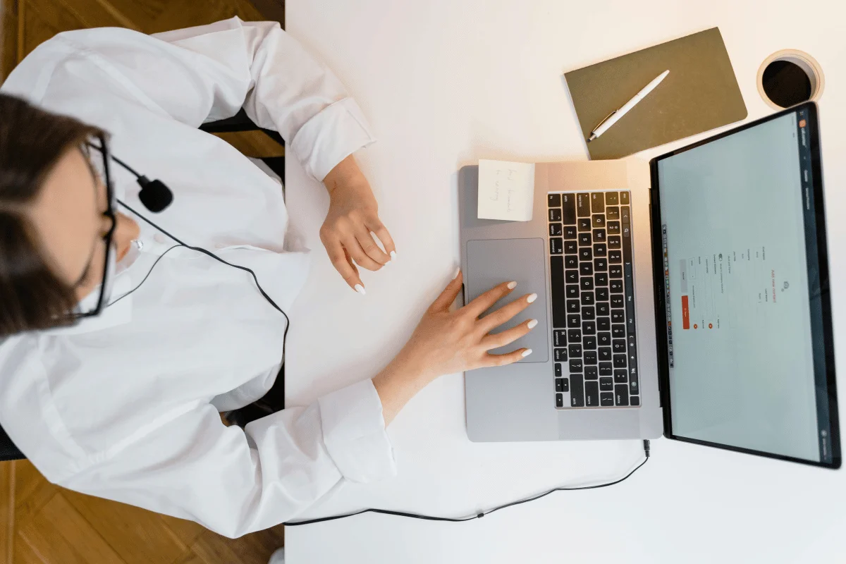 Woman in headset working on laptop during online communication.