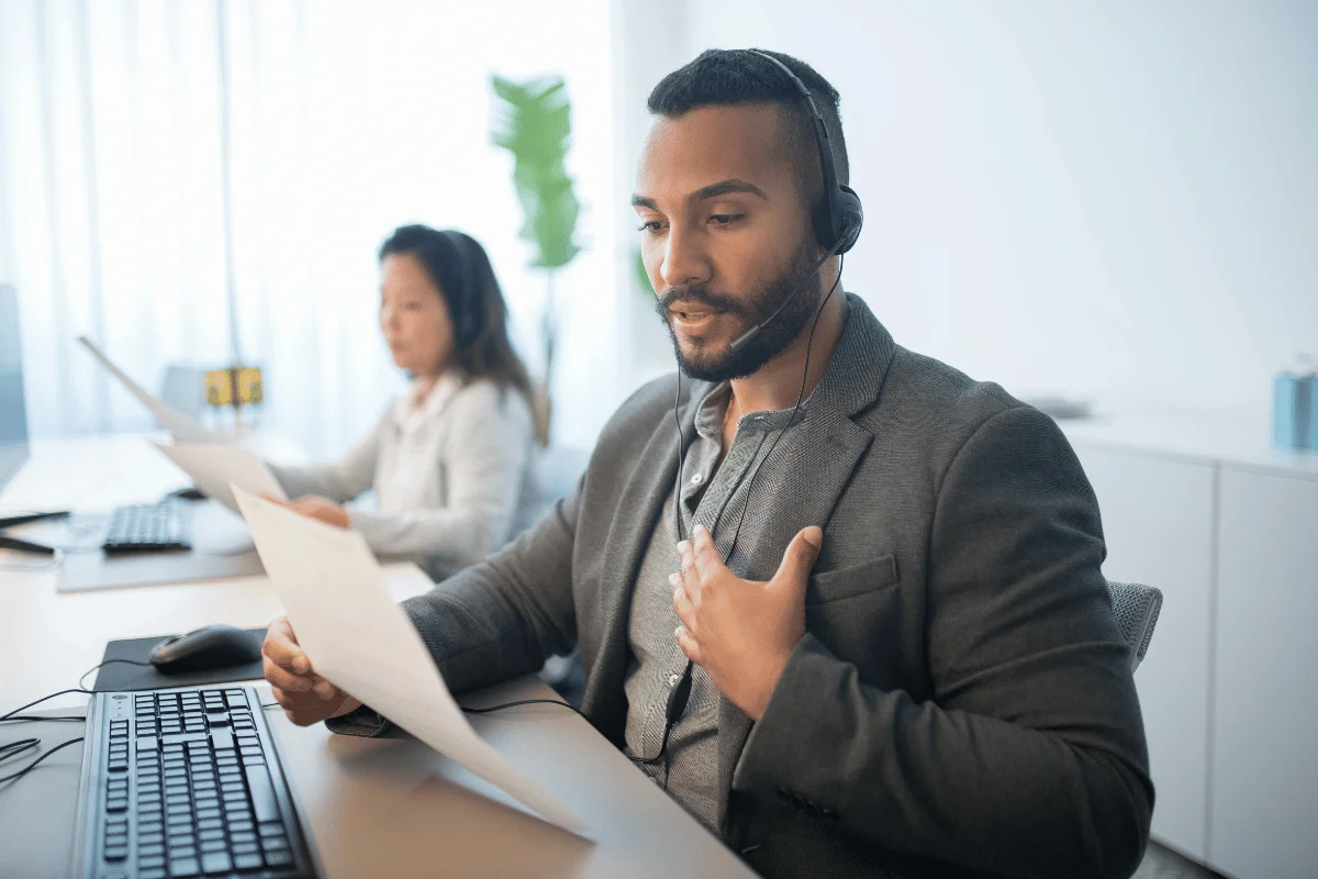 Customer service representative speaking on headset while reviewing documents.