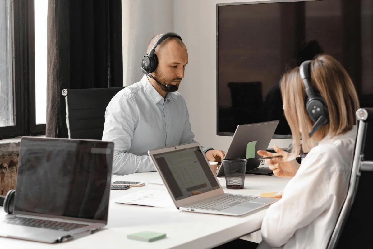 Man and woman wearing headsets during a remote support meeting in a modern office with laptops.