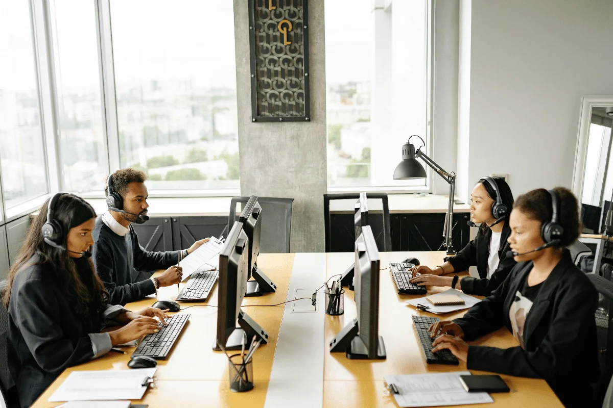 Diverse customer service team wearing headsets and working at desktop computers in a bright office.