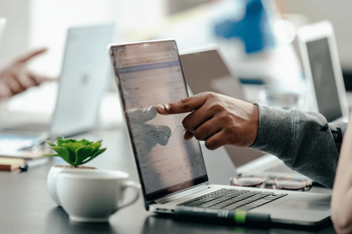 Close-up of a person pointing at performance data on a laptop screen.