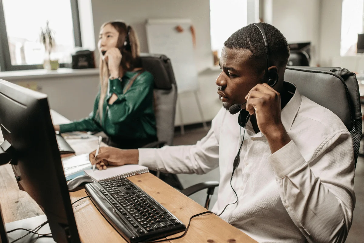 Call center agents wearing headsets while assisting customers on desktop computers.
