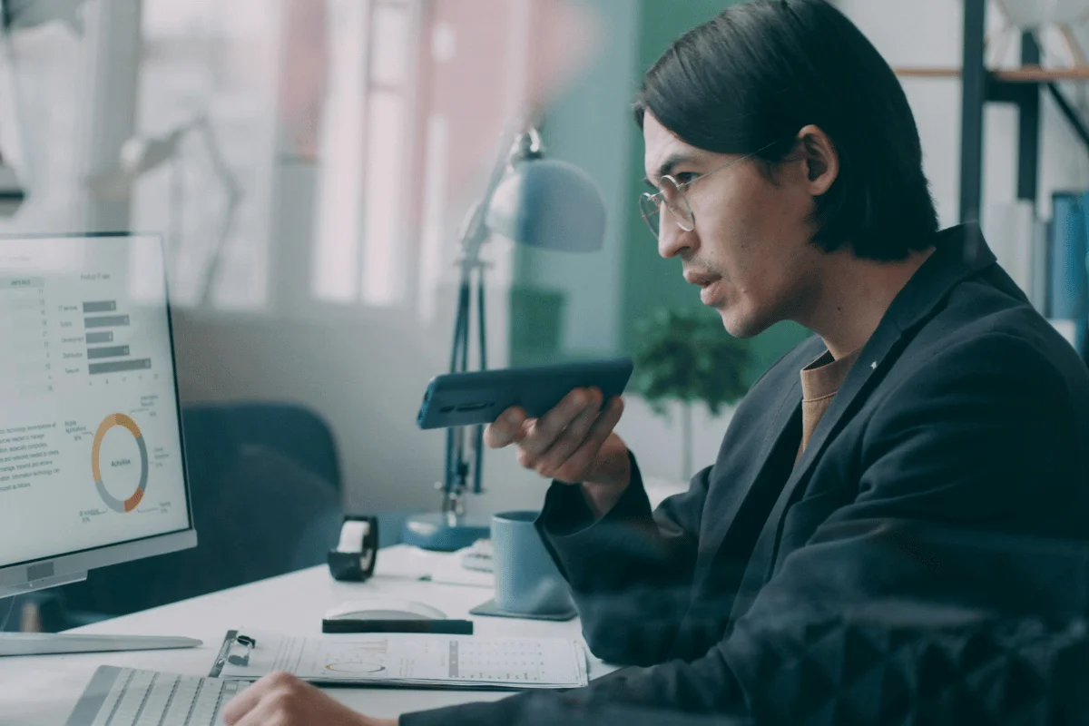 Businessman analyzing data dashboard while speaking into smartphone in modern office.