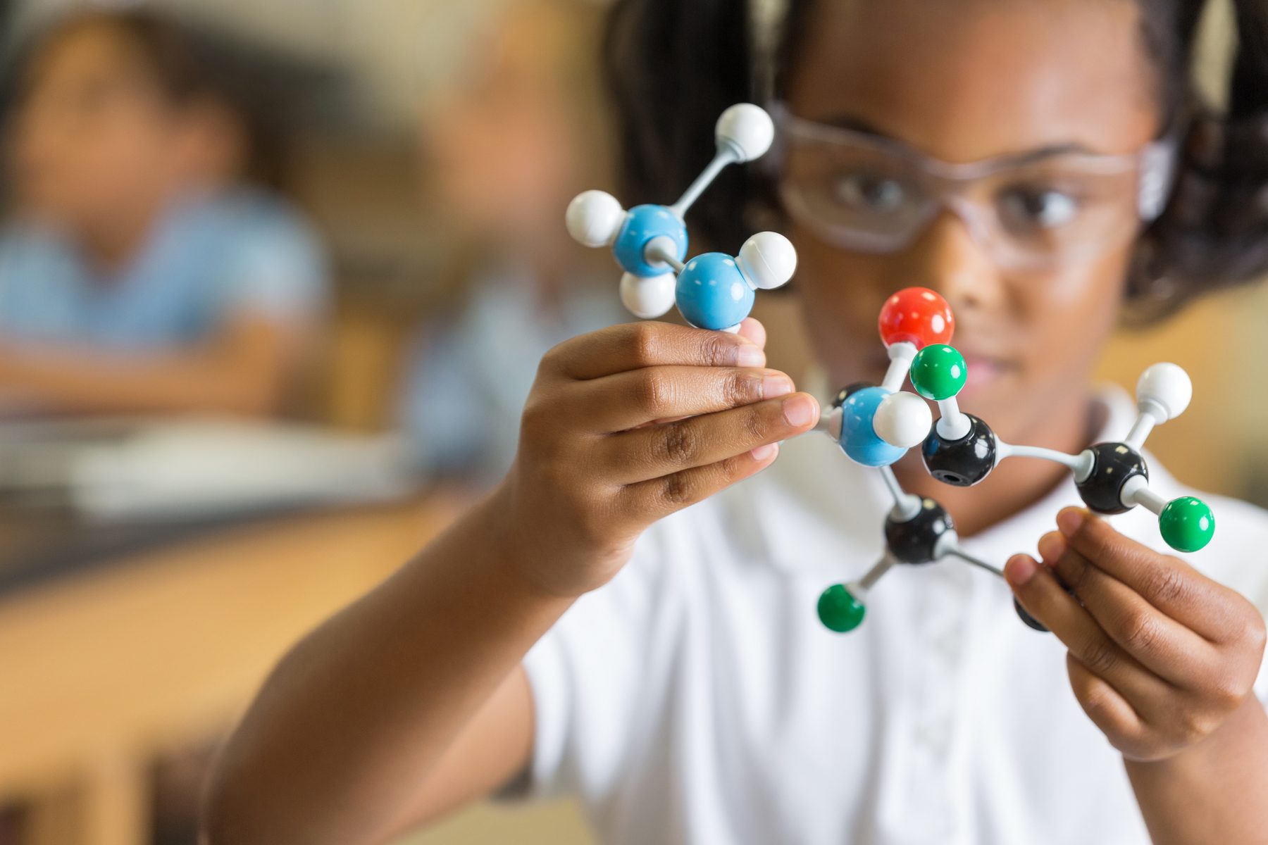 A student in safety goggles examining a ball-and-stick molecular model in a science classroom
