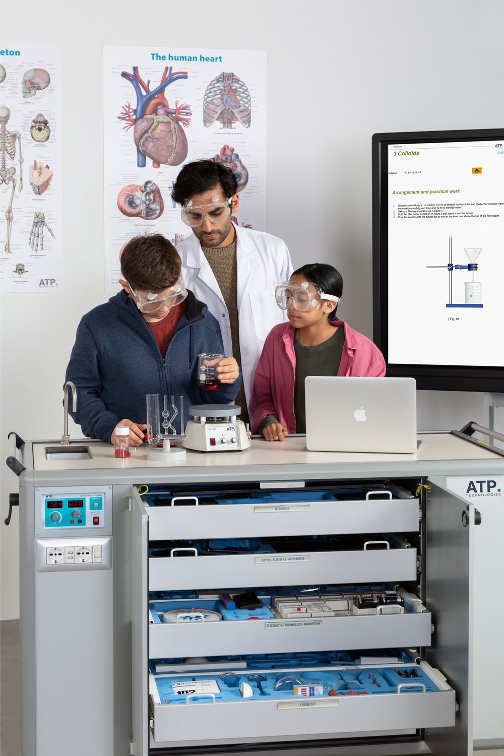 Un professeur et deux élèves portant des lunettes de protection réalisent une expérience de chimie sur le Mobile Lab d'ATP; les tiroirs de l'appareil, portant l'inscription « Smart Tray », sont ouverts en bas, et le guide de l'expérience s'affiche sur l'écran derrière eux.