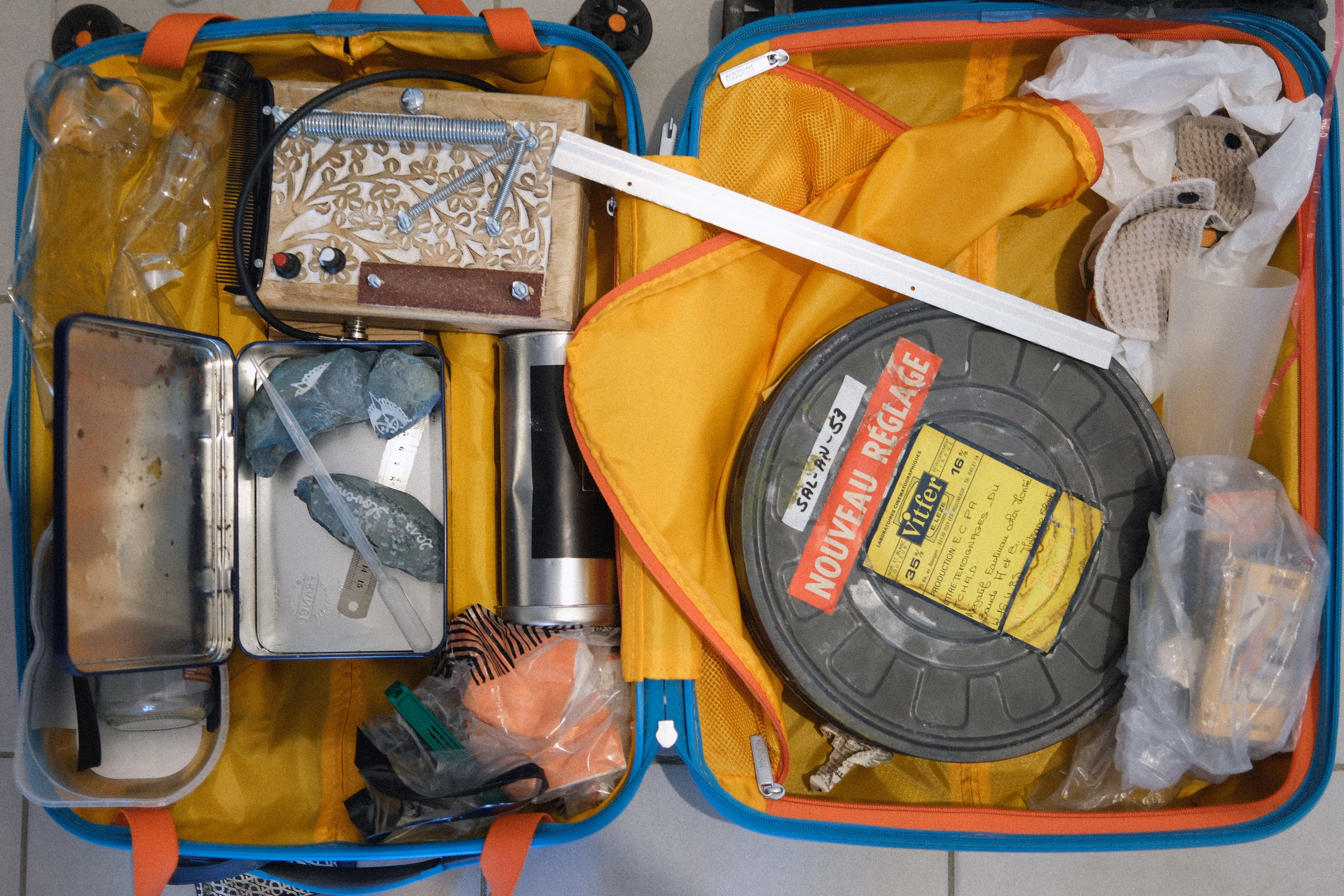 Valise ouverte contenant des objets hétéroclites utilisés pour la création sonore : boîte à musique artisanale, pierres, bobine de film, figurines en tissu et divers accessoires