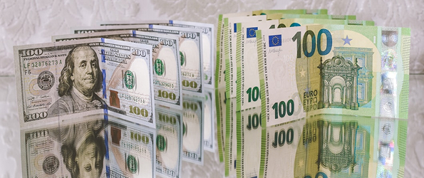 Stacks of US 100-dollar bills and 100-euro banknotes placed side by side on a reflective surface.