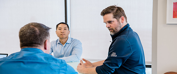 Three men having a discussion in an office setting.